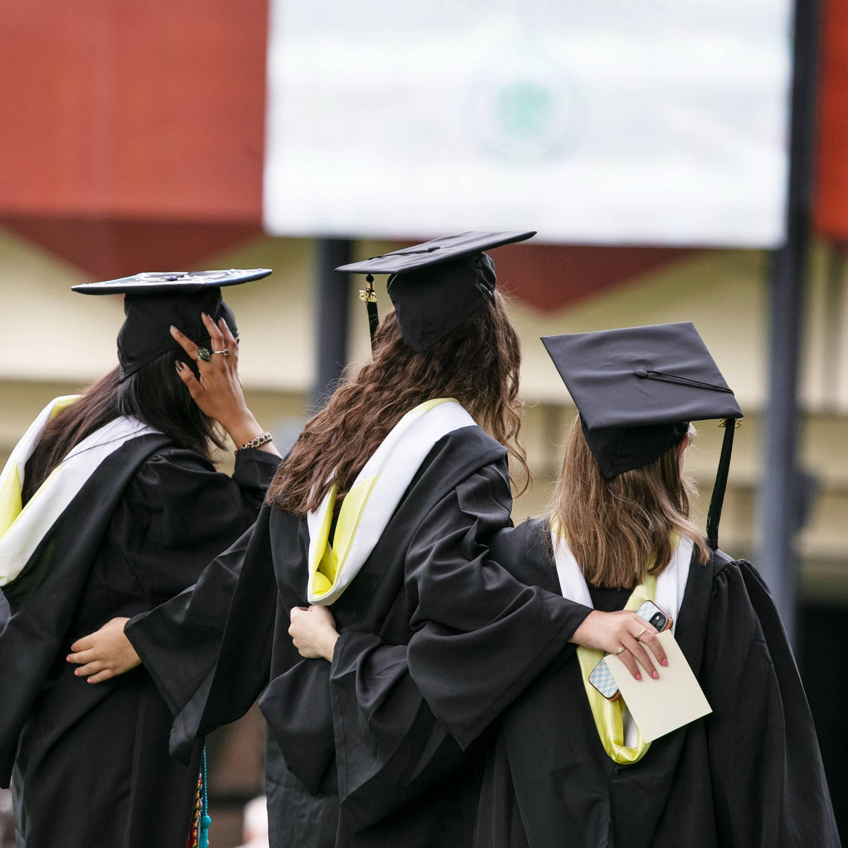 Three+Skidmore+graduates+face+away+from+the+camera+with+their+arms+around+each+other+during+2023+Commencement.+